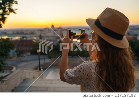 Young Woman on vacation using mobile phone to take photo of sunset of city. Rest, lifestyle concept. 117157198