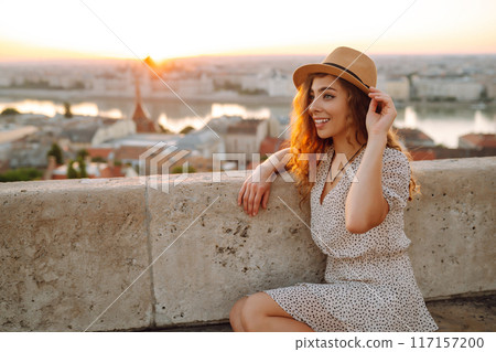Portrait of happy tourist in hat at dawn enjoys cityscape. Traveling in Europe. Concept tourism. 117157200