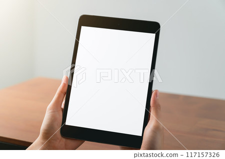 Hands holding digital tablet with mockup of blank screen on sofa in living room. Hands holding digital tablet with mockup of blank screen on sofa in living room. 117157326