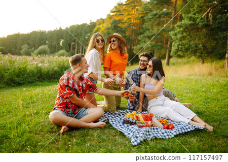 Stylish friends enjoy sunny day on beautiful green meadow. Vacation, friendship or holliday concept. Stylish friends enjoy sunny day on beautiful green meadow. Vacation, friendship or holliday concept. 117157497