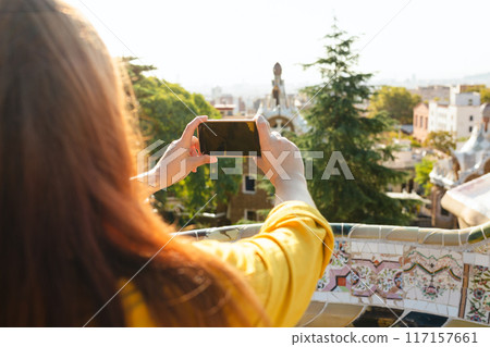 Redhead Woman taking picture of Barcelona from Guell Park. Concept of travel, tourism, technology and vacation in city. Rear view. Sunny day in city Redhead Woman taking picture of Barcelona from Guell Park. Concept of travel, tourism, technology and vacation in city. Rear view. Sunny day in city 117157661