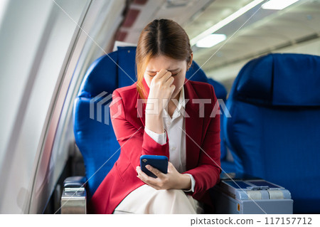 Tired businessman talking on the phone arguing work problems highlighting customer dissatisfaction while sitting in the airplane, Passengers near the window. 117157712