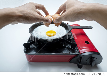 A person is cracking an egg into a pan on a stove A person is cracking an egg into a pan on a stove 117157818