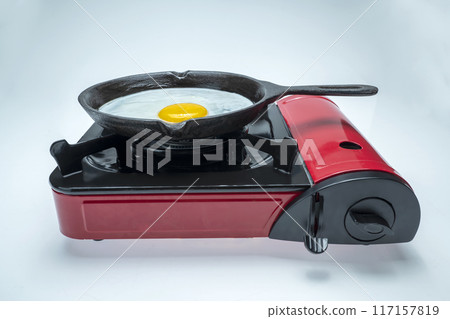 A red pan with a yellow egg in it sits on top of a red stove A red pan with a yellow egg in it sits on top of a red stove 117157819