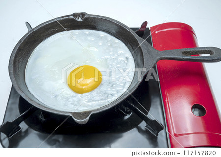 A red pan with a yellow egg in it sits on top of a red stove A red pan with a yellow egg in it sits on top of a red stove 117157820