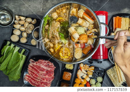 A person is holding a spoon in a large pot of food A person is holding a spoon in a large pot of food 117157839