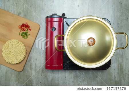 A red pot with a gold lid sits on top of a burner 117157876