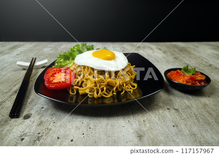 A plate of instant noodles with an egg on top and a tomato slice 117157967