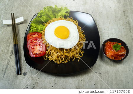 A plate of instant noodles with an egg on top and a tomato slice 117157968
