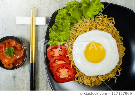 A plate of instant noodles with an egg on top and a tomato slice 117157969
