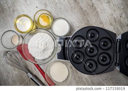 A red and silver whisk is on a table with other kitchen items 117158019