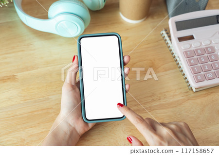 Female hands holding smartphone with mockup of blank screen on desk in office room. 117158657