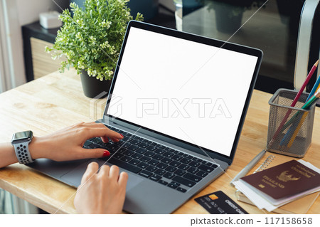 Woman hand using laptop and typing on keyboard with mockup of blank screen on wooden table. 117158658