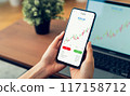 Businessman trader using smartphone with stock market investments and graph on screen to analyze trading data, buy or sell and checking price on mobile application. 117158712