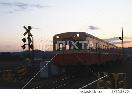 夕陽下穿過鐵路道口的當地火車和警報系統的輪廓 117158870