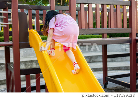 Cute asian girl playing on the slide in the playground Cute asian girl playing on the slide in the playground 117159128