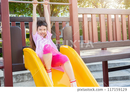 Cute asian girl playing on the slide in the playground Cute asian girl playing on the slide in the playground 117159129