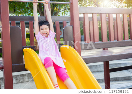 Cute asian girl playing on the slide in the playground Cute asian girl playing on the slide in the playground 117159131