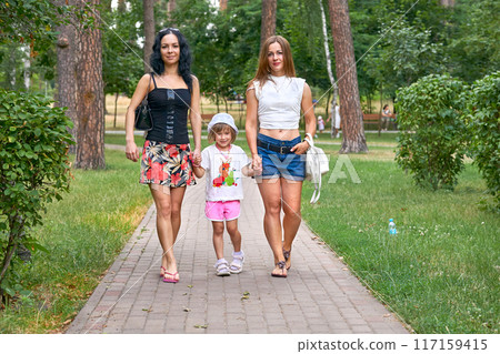 Two young women with a girl child are walking in a summer park Two young women with a girl child are walking in a summer park 117159415