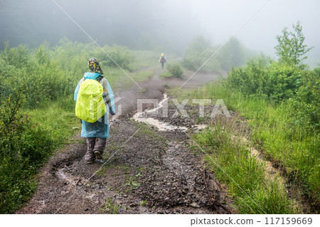 Tourist in raincoat hikes to mountain in the fog Tourist in raincoat hikes to mountain in the fog 117159669