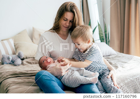 A young mother with two small children spends time in the bedroom at home.	 117160796