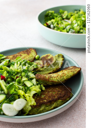 Zucchini and broccoli pancakes served with a mixed salad of cucumbers, young peas, and radishes 117162060