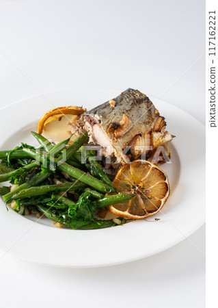 This savory dish features baked green beans with onions and tender mackerel, served on a plate against a white background, offering a healthy This savory dish features baked green beans with onions and tender mackerel, served on a plate against a white background, offering a healthy 117162221