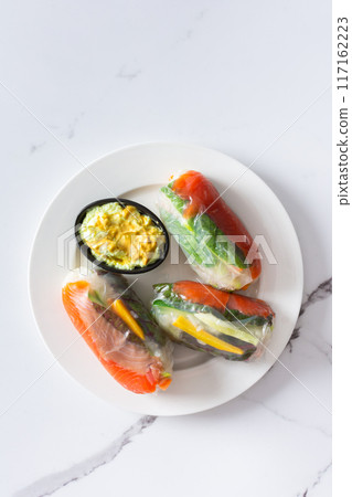 These traditional Vietnamese spring rolls feature rice paper filled with lettuce, salmon, carrots, and cucumber, served with fish sauce, offering a light and flavorful appetizer 117162223