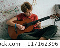 Romantic adolescent redhead girl learning to play the guitar while sitting in the room.	 117162396