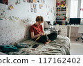 Teenage girl doing homework while sitting in the room.	 117162402