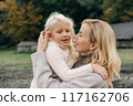 Mom holds in her arms and hugs a little blond cheerful daughter.	 117162706