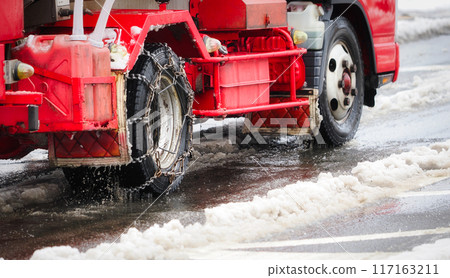 A truck with tire chains driving on a slushy snow road 117163211