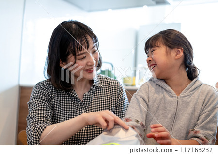 A mother and daughter laughing as they put their hands into a knapsack A mother and daughter laughing as they put their hands into a knapsack 117163232