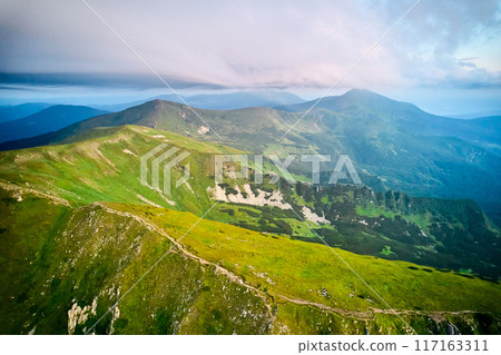 Breathtaking aerial view of green, rugged mountain peaks under dramatic sky. Scene captures contrast between vibrant landscape and moody clouds, with sunlight breaking through. Carpathians, Chornogora Breathtaking aerial view of green, rugged mountain peaks under dramatic sky. Scene captures contrast between vibrant landscape and moody clouds, with sunlight breaking through. Carpathians, Chornogora 117163311