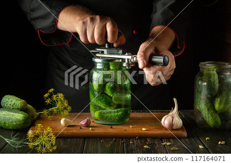 Preserving cucumbers in a jar with spices. A chef uses a hand seamer to seal a jar of pickled cucumbers 117164071