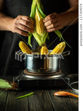 A cook peels a corn cob on the kitchen counter before boiling it in a pot. Concept of cooking maize for a restaurant lunch. Corn diet A cook peels a corn cob on the kitchen counter before boiling it in a pot. Concept of cooking maize for a restaurant lunch. Corn diet 117164074