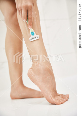 Young woman shaving her legs with razor in white shower, close-up Young woman shaving her legs with razor in white shower, close-up 117164946