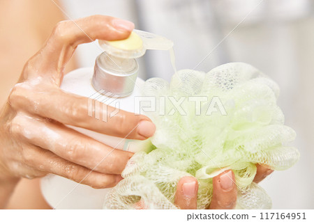 female hands pouring liquid moisturizing soap shower gel from white cosmetic bottle on sponge in bathroom 117164951