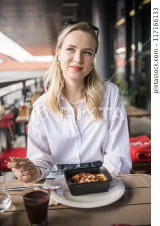 Blonde gen z woman eating lasagna in the cafe on break. Gen z girl spend time in restaurant 117166133