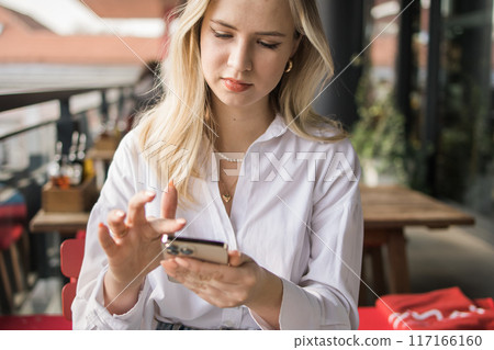 Restaurant and smartphone. Close-up relaxed blond woman typing and scroll or check email and contact social media app or social network user. Happy smile and young gen z girl with mobile tech post to 117166160