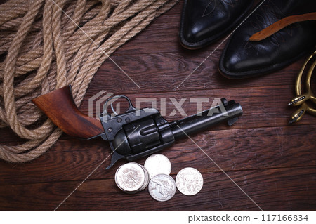 Old western revolver gun with silver dollars and cowboy boots 117166834