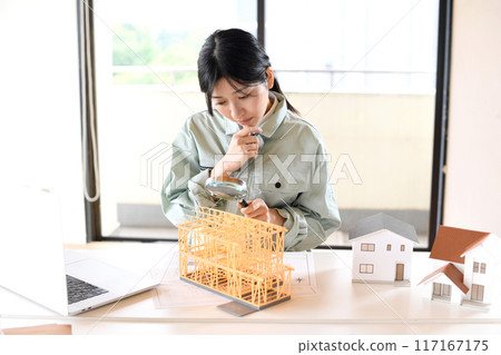 一位穿著工作服的年輕女子用放大鏡看著房屋模型 117167175