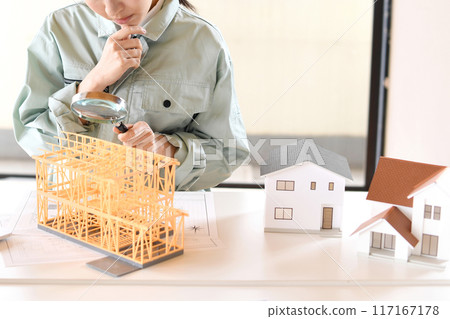 一位穿著工作服的年輕女子用放大鏡看著房屋模型 117167178