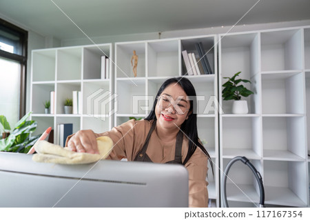 Cheerful Housekeeper Cleaning Modern Home Office with Bookshelves and Plants in Background 117167354