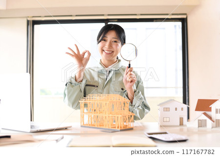 穿著工作服的女人在房屋模型前拿著放大鏡 117167782
