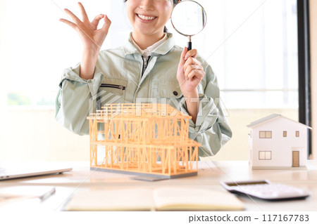 穿著工作服的女人在房屋模型前拿著放大鏡 117167783