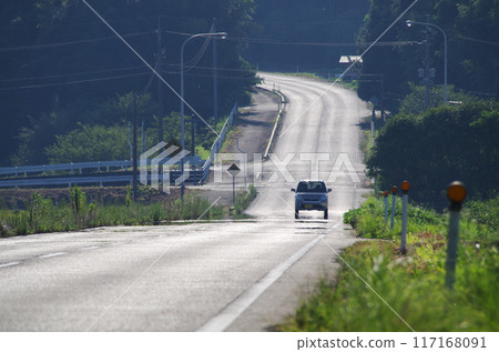 A light vehicle running on an asphalt road under the scorching sun 117168091