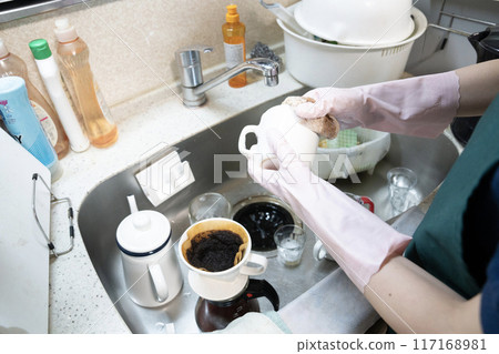 A female housecleaning staff member tidies up a messy kitchen A female housecleaning staff member tidies up a messy kitchen 117168981