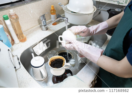 A female housecleaning staff member tidies up a messy kitchen 117168982
