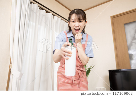 A woman spraying insecticide in the living room 117169062